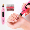 Een persoon gebruikt de Fashiongirl Electric Nail File 6-in-1 Manicure Set in roze op haar vingernagels, met de meegeleverde boortjes en schuurbandjes naast het gereedschap.