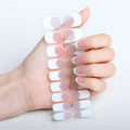 Een hand met gemanicuurde nagels houdt UNIQ Semi Cured Gel Nail Stickers / Zelfklevende nagellak - Classic French (JK-331) vast, met een chique wit en lichtroze halve maanontwerp dat perfect bij de nagels past.