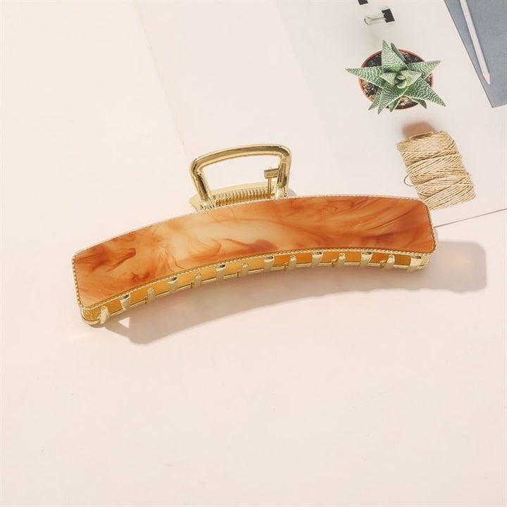 The SOHO Abby Hair Claw - Ginger by SOHO, featuring a marbled light brown design, rests on a white surface beside a potted succulent, twine, and a magazine—ideal for secure hair styling and daily wear.