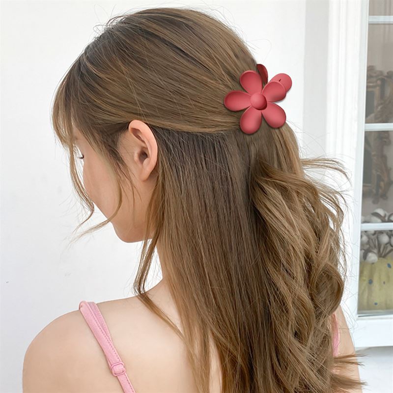 A woman with long, wavy light brown hair is seen from behind indoors, wearing a SOHO Bloom Hair Claw - Peach by SOHO and a pink spaghetti strap top near a window.
