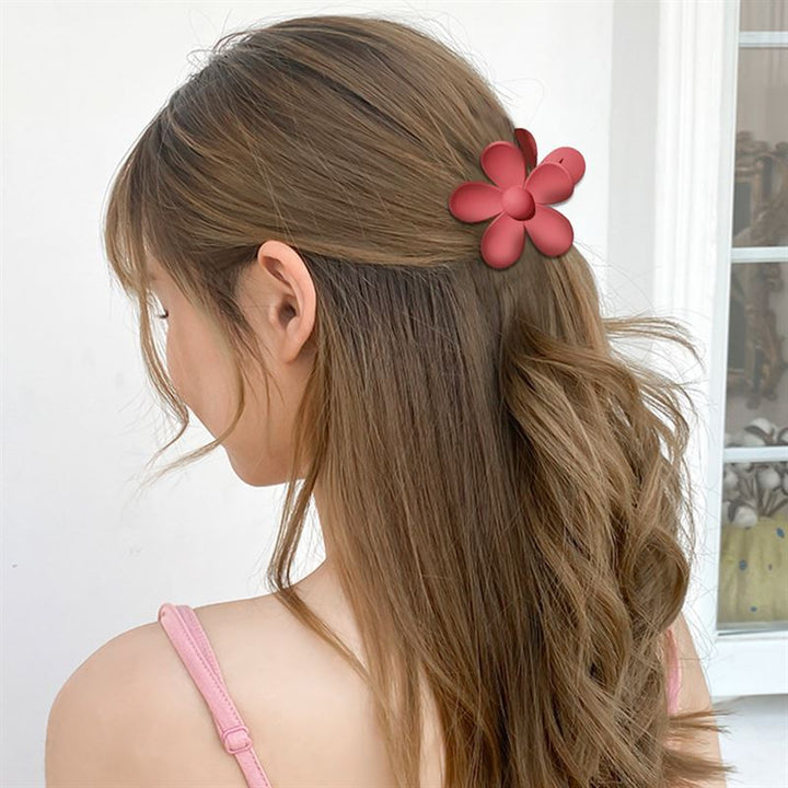 A woman with long, wavy light brown hair is seen from behind indoors, wearing a SOHO Bloom Hair Claw - Peach by SOHO and a pink spaghetti strap top near a window.