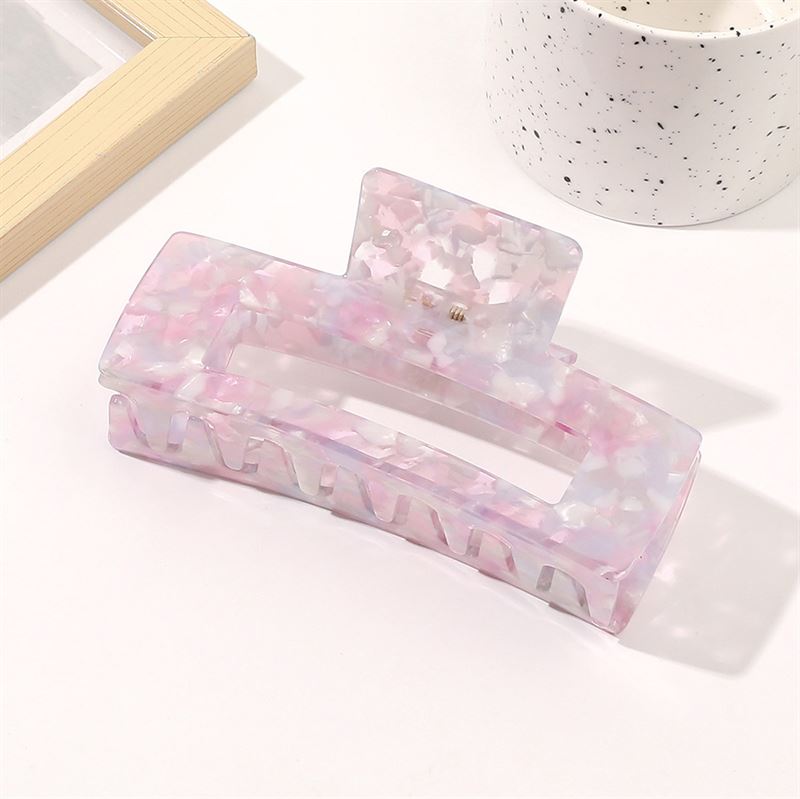 The SOHO Clara Hair Claw in Lavender Pink, an XL rectangular clip, rests on a white surface beside a speckled white cup and a wooden photo frame.