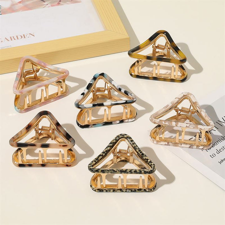 Six SOHO Ea Hair Claw - Marble clips by SOHO, featuring gold bases and vibrant patterns like pink, tortoiseshell, and animal print, are displayed on a white surface beside a framed picture and magazine—a chic accessory arrangement.