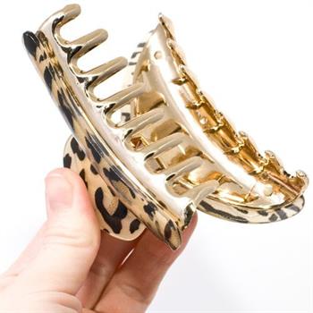A hand holds the SOHO Hair Claw - Leopard by SOHO, a large gold and black acrylic hair clip with a leopard motif, against a plain white background.