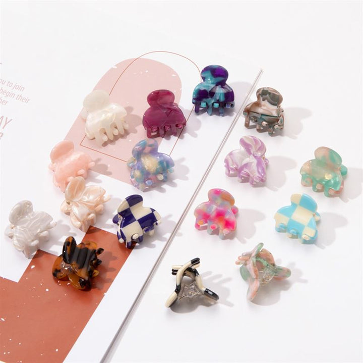 SOHO Hara Mini Hair Claw - Beach by SOHO features colorful mini hair claws in assorted patterns and designs, neatly arranged on a white and pink surface to highlight their unique shapes, vibrant colors, and secure grip.
