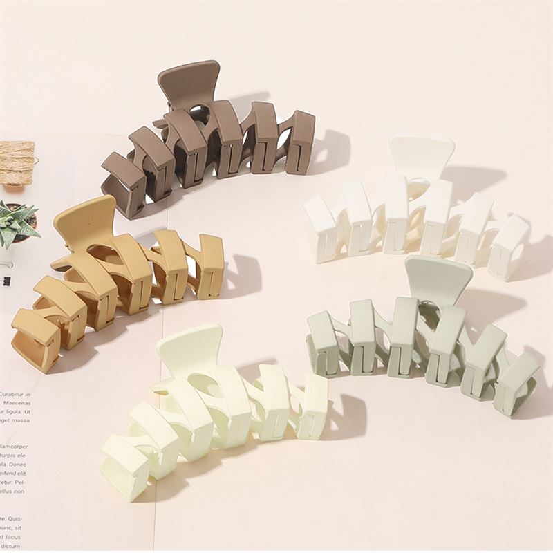 The SOHO Just Hair Claw in Brown by SOHO, shown with other matte claws in neutral shades on a light surface near an open magazine, is the perfect everyday hair accessory.