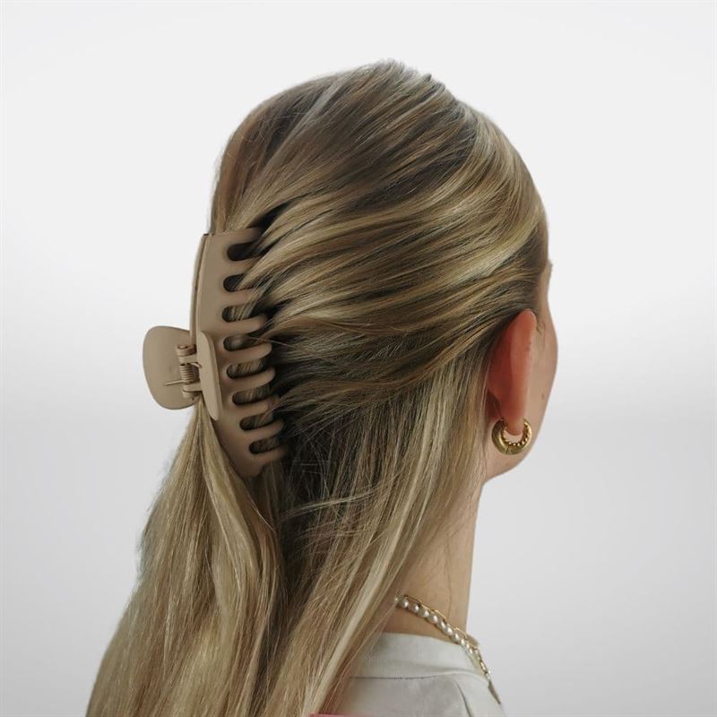 A woman with blonde hair in a half-up style, secured by the SOHO Kana Hair Claw - Beige, known for its strong grip. She wears gold hoop earrings and a chain necklace, facing away—ideal for all hair types. Brand: SOHO.