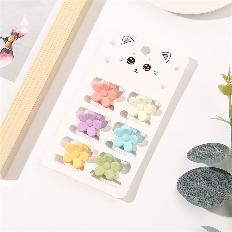 The SOHO Lala Mini Hair Claws - Pastel Flowers set features eight flower-shaped pastel hair claws in pink, purple, yellow, blue, and green. Displayed on a white card with a cute cat face by SOHO, and surrounded by leaves and papers.