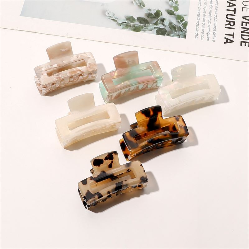 The SOHO Leia Mini Hair Claw in Beige Marble from SOHO is beautifully showcased on a white surface near a magazine and a green plant, ideal for effortless hairstyling.