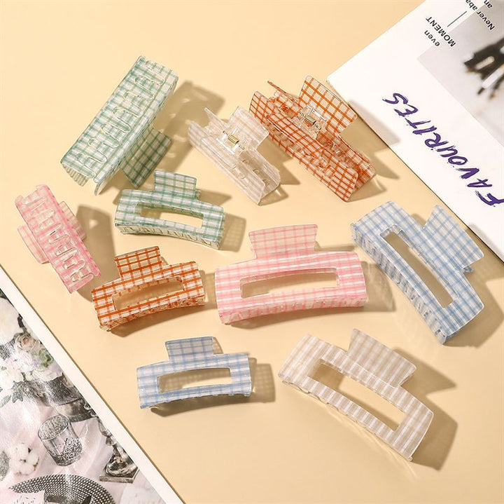 The SOHO Line Hair Claw - Green by SOHO features a colorful plaid design and offers a secure hold, making it a stylish hair accessory for any look. Pictured on a beige surface beside a magazine and floral-patterned fabric.