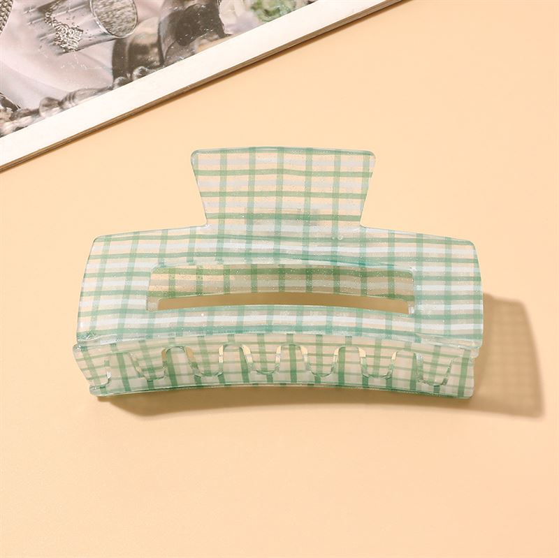 The SOHO Line Hair Claw in pastel green and white by SOHO rests on a light beige surface near a magazine corner, blending secure hold with stylish flair.