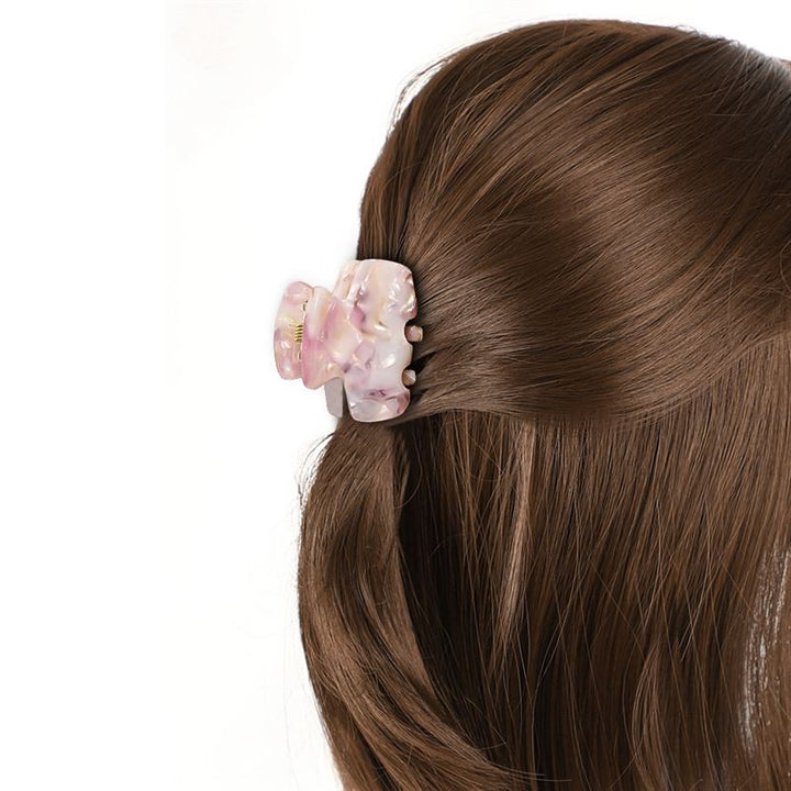 A close-up of brown hair partially pulled back with the SOHO Loa Mini Hair Claw - Blush. The shiny strands are neatly held, while the stylish SOHO clip grips a small side section for an elegant touch.
