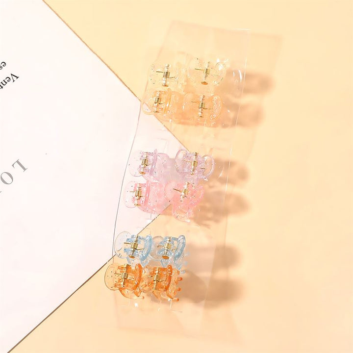 De SOHO Lucca Mini Hair Claws - Glitter van SOHO hebben pastelgele, roze en blauwe ontwerpen op een doorzichtige strip, wat een charmante touch aan je stijl toevoegt. Ze worden op beige naast wit papier getoond voor een stijlvolle presentatie.