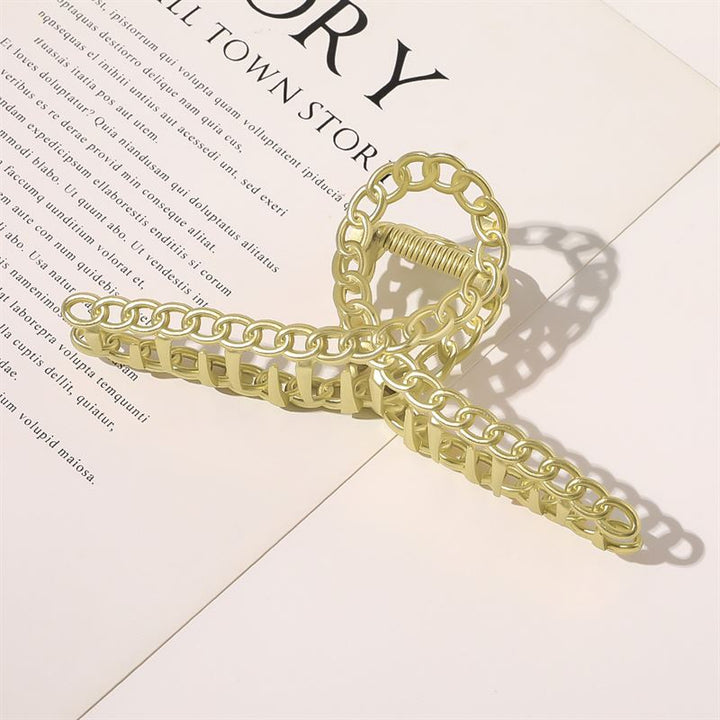 The SOHO Monz Metal Hair Claw in gold by SOHO sits atop an open book, casting a delicate shadow over English and foreign text—a sophisticated hair accessory that elevates your reading experience.