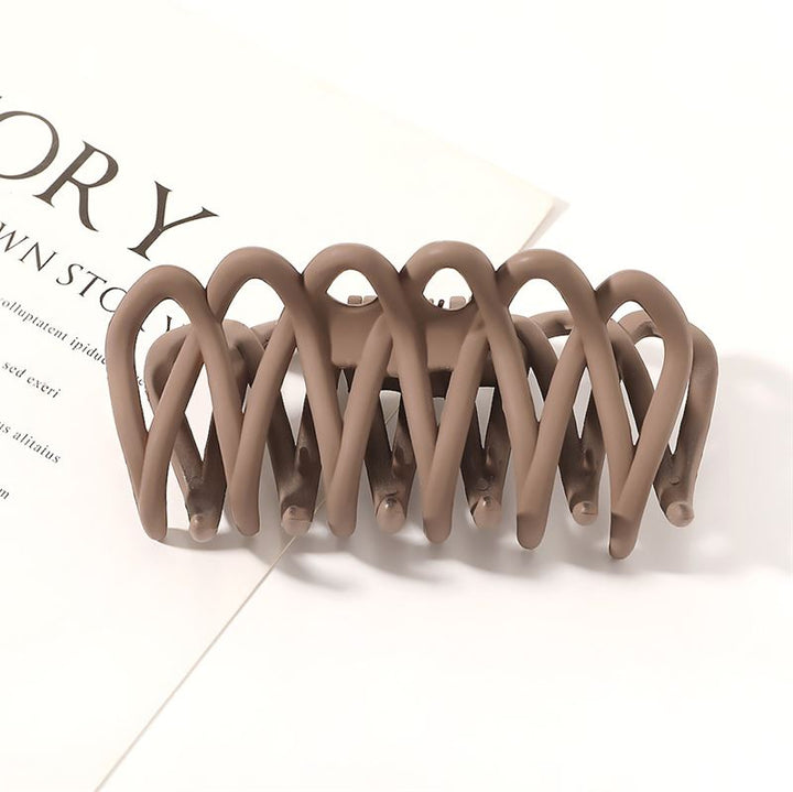 The SOHO Olive Hair Claw - Brown by SOHO features a matte, interwoven curved design and gentle grip, shown resting on a white surface near printed text—ideal for securing all hair types.