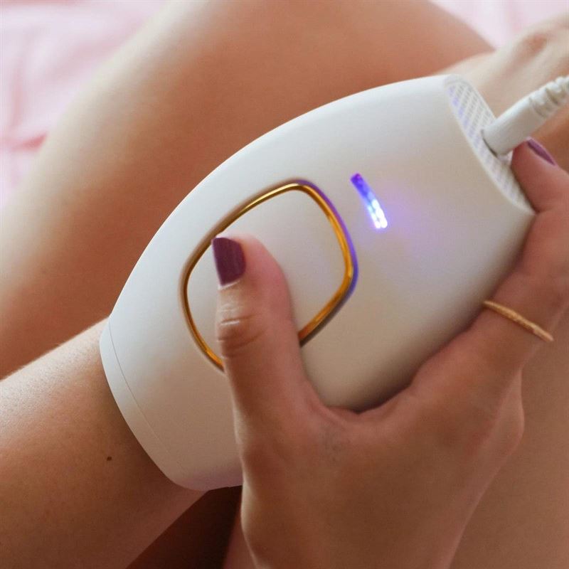 A person with painted nails uses the UNIQ IPL Hair Removal Device—featuring a glowing blue indicator—for smooth, pain-free, permanent hair reduction at home.